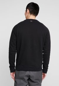 Sudadera negra de tejido suave, con un cuello y puños acanalados, y un pequeño logo en la parte superior de la espalda. Diseño simple y limpio.