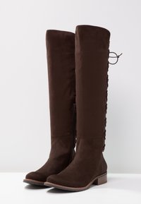 Hnědé semišové kozačky nad kolena s bočním zipem a šněrováním na zadní straně. Zaoblená špička a nízký blokový podpatek.