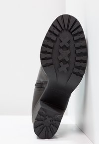 Zwarte laars met een gestructureerde rubberen zool, voorzien van een zigzagprofiel en een zijrits. Gladde leren bovenkant met subtiele stikdetails.