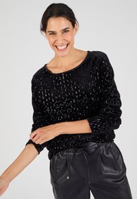 Suéter negro con lentejuelas, de corte suelto, escote redondo, tejido texturizado, mangas largas y dobladillo fruncido, combinado con pantalones de cuero negros.