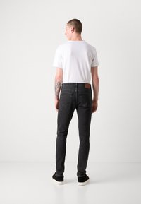 Jeans oscuros con un corte slim, un parche de cuero marrón en la parte trasera, combinados con una camiseta blanca y zapatos negros. Textura suave y diseño minimalista.