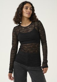 Black lace long-sleeve top with layered texture, fitted design, and crew neckline, paired with high-waisted black jeans.