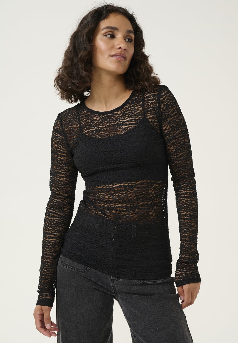 Black lace long-sleeve top with layered texture, fitted design, and crew neckline, paired with high-waisted black jeans.