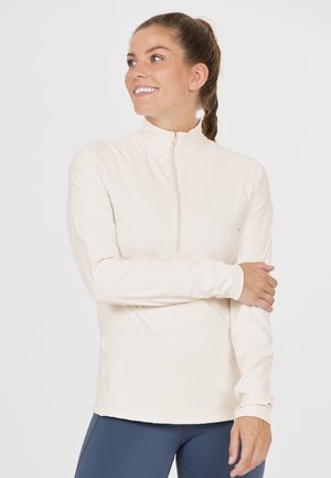 Hellbeige, tragbare, langärmlige Sportjacke mit Reißverschluss, die einen hohen Kragen und eine taillierte Passform bietet, ideal für Aktivitäten. Sanfte Textur.
