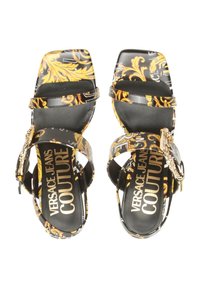 Sandales à talons hauts noires et jaunes à motifs avec deux brides, logo sur la semelle intérieure et accent chaîne décoratif sur le côté.