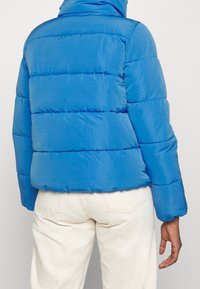 Blå puffjacka, kviltad design, hög krage, ribbade muddar, syntetiskt material, med synlig horisontell sömnad och elastisk fåll.