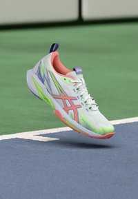 Λευκό αθλητικό παπούτσι με πράσινες και ροζ λεπτομέρειες, ανθεκτικό υφαντό επάνω μέρος και ευέλικτη σόλα, σχεδιασμένο για αποδοτικότητα σε γήπεδα.