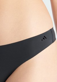 Schwarze Bikini-Unterteile aus glattem Stoff; verfügen über einen breiten Bund und drei Ausschnitte auf einer Seite für zusätzliche Designdetails.