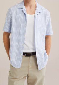 Kortärmad skjorta med knappar i ljusblått med vita vertikala ränder. Tillverkad av textil med struktur, har en camp collar och rak nederkant.