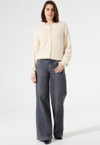 Cremfarbener, fluffiger Cardigan mit rundem Ausschnitt und Knopfverschluss, kombiniert mit dunkelgrauen, weit geschnittenen Jeans. Einfaches Design, lässige Passform, keine Verzierungen.