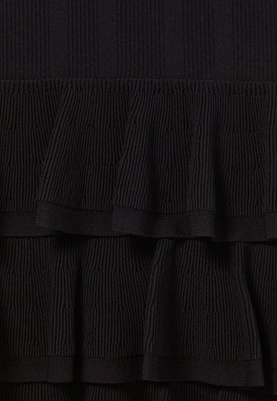 Il tessuto lavorato a maglia nero presenta un design testurizzato con tre livelli di ruches. Il motivo è composto da righe orizzontali che si estendono in tutta la superficie.