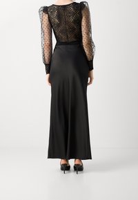 Abito da sera nero con un corpetto in tulle trasparente a pois, dettagli in pizzo e una gonna in satin liscia, con maniche a sbuffo lunghe e una silhouette aderente.