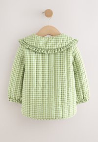 Grüne Steppjacke mit Vichy-Karomuster, Rüschenkragen und elastischen Bündchen, mit weicher Textur und abgerundetem Saum, an einem Holzkleiderbügel hängend.