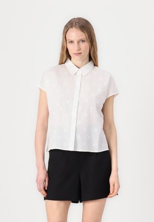 Chemise blanche à manches courtes avec un devant à boutons, ornée de broderies florales et d'un col. Associée à un short noir.