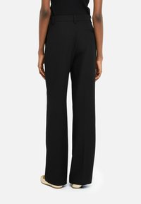 Pantaloni neri a gamba larga caratterizzati da un tessuto morbido, una vita sartoriale e due tasche posteriori, con un design pulito e minimalista.