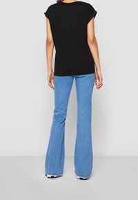 Černé bavlněné tričko s krátkými rukávy, které jsou ohrnuté, v kombinaci s modrými zvonovými džíny, které mají mírný elastický efekt a roztrhaný lem.