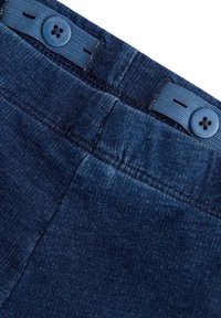 Mörk denimbyxor med en texturerad yta, två blå knappar i midjan och en sydd design längs kanterna.
