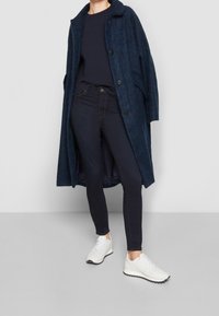 Abrigo de mezcla de lana en color navy con corte oversized, grandes botones y bolsillos laterales, sobre una camiseta navy, combinado con jeans oscuros y zapatillas blancas.
