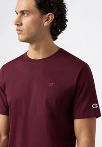T-shirt bordeaux a maniche corte in cotone con colletto a girocollo, dotato di un piccolo logo ricamato sul petto e di un logo a contrasto sulla manica.