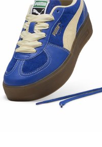 Baskets Puma bleu et crème avec des lacets en satin crème, des lacets bleus supplémentaires à côté et une semelle marron texturée.