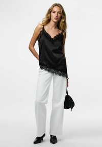 Svart satengkamisole med blonder langs utringningen og kanten, kombinert med hvite vidbukser og svarte sko med spiss tå.