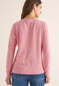 Camisa de manga larga rosa con un patrón de punto texturizado, escote redondo y corte relajado. Combinada con jeans azules, se puede ver la parte de atrás.