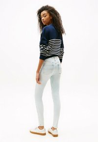 Suéter de rayas en navy con un corte relajado, combinado con jeans skinny de color azul claro y zapatillas blancas con suela en tono marrón. Cabello rizado visible.