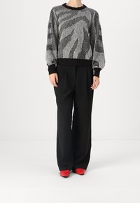 Tröja i svart och vitt med texturerat mönster och långa puffärmar, i kombination med vida svarta byxor och röda skor.