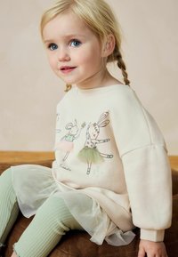 Vaaleanbeige neulepaita, jossa on leikkisiä pupu-illustratioita ja pastellinvärisiä tyllikoristeita. Ribattu mintunvihreä legginsit ja kerroksellinen tyllihame.