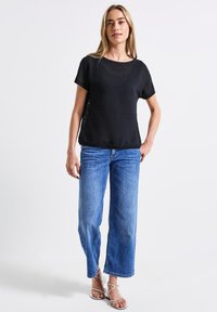 Top negro de manga corta con un patrón texturizado, combinado con jeans de pierna ancha en azul claro y sandalias blancas de tiras. Estilo minimalista.