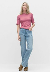Różowa, teksturowana bluzka z krótkim rękawem w połączeniu z jasnoniebieskimi dżinsami typu flare i brązowymi botkami za kostkę. Prosty design, casualowy krój i miękkie materiały.