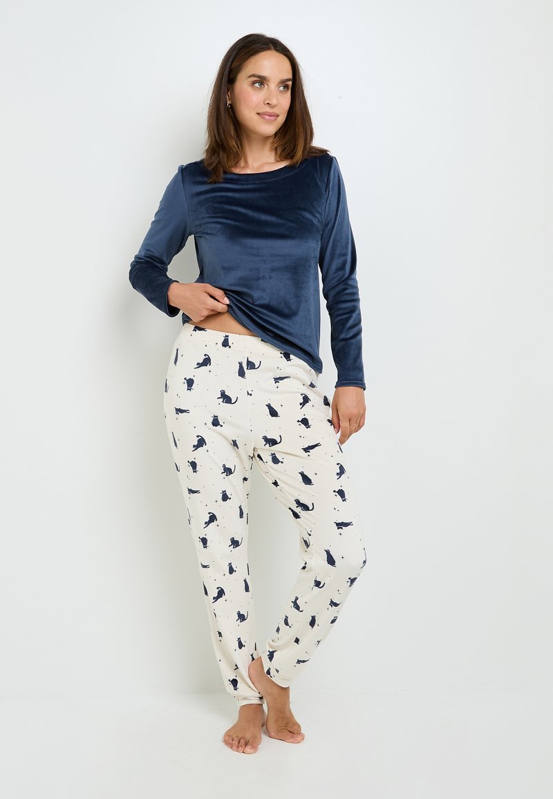 Top manica lunga in velluto blu navy abbinato a pantaloni crema con silhouette di gatti blu navy. Tessuto morbido, vestibilità rilassata, vita elastica.