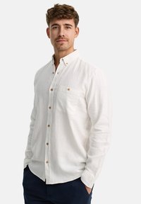 Camisa de lino blanca de manga larga con cuello abotonado, un bolsillo en el pecho y botones de madera; ajuste relajado y tejido texturizado.