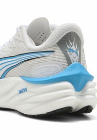 White athletic shoe with blue accents; mesh upper, padded collar, and chunky textured sole featuring a distinctive wave pattern.