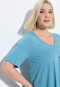 Modrá krátká rukávová blůza s kulatým výstřihem, vyrobená z měkké tkaniny. Má volný střih a prošití na přední straně.