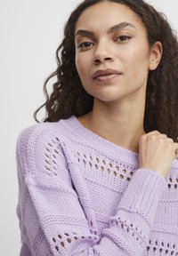 Svetor iz lilac volne z širokim dekoltejem, ki se ponaša z teksturiranim dizajnom in odprtinami, rebrastimi manšetami ter sproščenim krojem.