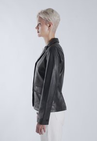 Čierny kožený blazer s priliehavým strihom, s klopovým golierom, dvoma prednými vreckami a gombíkovými manžetami. Hladká textúra, moderná silueta.