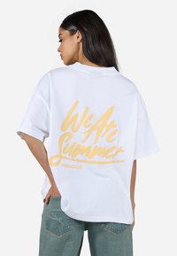 Hvit oversized t-skjorte med gul tekst "We Are Summer" og "PEGADOR" trykt på baksiden. Mykt stoff, korte ermer, avslappet passform.