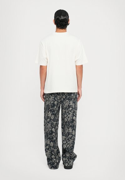 Tricou alb din bumbac și pantaloni negri evazați cu un model floral. Ținuta are o croială lejeră și o textură moale.