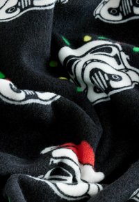 Fekete gyapjú takaró, amelyen fehér rohamosztagos sisakok mintája látható piros és zöld ünnepi részletekkel. Puha tapintású, meleg megjelenésű.