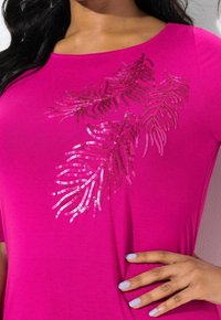 Top rosa de manga corta con un diseño de hojas de lentejuelas en tonos más oscuros de rosa. Tejido suave con un corte relajado, escote redondo y un suave brillo.