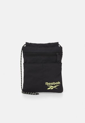 Pochette à cordon noire Reebok avec poche avant zippée et logo Reebok jaune sur fond uni.