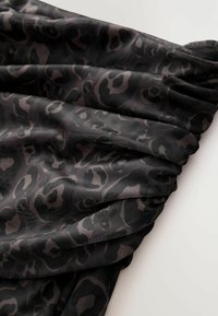Černá tkanina s jemným vzorem leopardích skvrn, s měkkými sklady a hladkou texturou. Design kombinuje tmavé a světlé odstíny pro kontrast.
