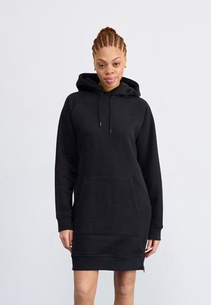 Vestido de sudadera negro con capucha, gran bolsillo frontal y puños acanalados. Presenta un corte ligeramente oversized y una cremallera en el dobladillo.