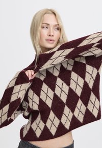Maglione a rombi nei colori marrone e crema, realizzato in tessuto lavorato a maglia, con collo alto e maniche ampie.