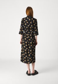 Pikk must kleit lillemustriga, kus on oranžid ja valged õied. Kleit on 3/4-sleeve'idega, seotud talje ja sirge siluetiga.