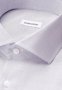 Camicia bianca in tessuto con un motivo a piccoli quadretti neri. Presenta un colletto rigido e un'etichetta Seidensticker vicino al colletto con due bottoni.