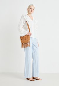 Hvit bluse med volanger, lyseblå stripete vide bukser og brun semsket crossover-veske med frynse detaljer. Flaue sandaler fullfører antrekket.