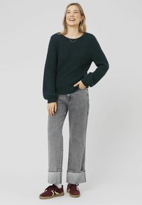 Pull en tricot côtelé vert foncé avec des manches longues, associé à un jean large taille haute gris et des baskets bordeaux.