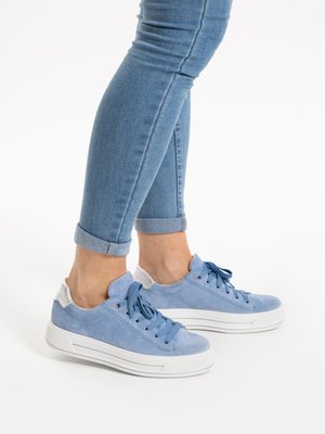 Person wearing light blue sneakers with white soles and rolled-up skinny jeans standing on a white surface.